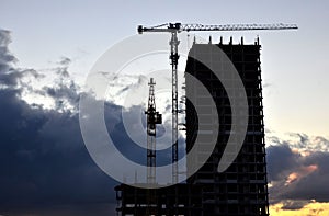 Jib construction tower crane and new residential buildings at a construction site on the sunset and blue sky background