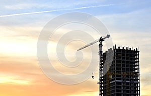 Jib construction tower crane and new residential buildings at a construction site on the sunset and blue sky background
