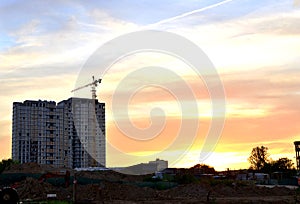 Jib construction tower crane and new residential buildings at a construction site on the sunset and blue sky background