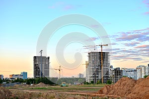 Jib construction tower crane and new residential buildings at a construction site on the sunset and blue sky background