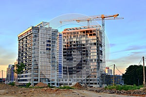 Jib construction tower crane and new residential buildings at a construction site on the sunset and blue sky background