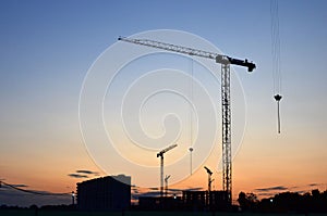 Jib construction tower cranes at a construction site on the sunset and blue sky background