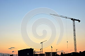 Jib construction tower cranes at a construction site on the sunset and blue sky background