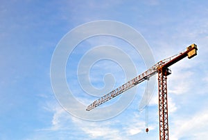 Jib tower crane at a construction site on the blue sky background