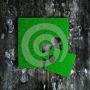 Jigsaw puzzles made out of green grass, on grunge dark concrete floor background
