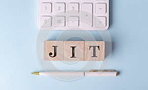 JIT on wooden cubes with pen and calculator, financial concept