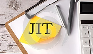 JIT word on a yellow sticky with calculator, pen and clipboard