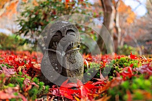 A Jizo statue with a smiling face is sitting on a pile of red leaves