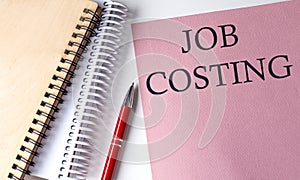 JOB COSTING word on the pink paper with office tools on white background