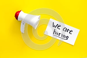 Job recruiting advertisement. We are hiring lettering near megaphone on yellow background top view copy space