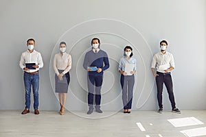 Job seekers in face masks waiting for job interview standing in corridor keeping safe distance