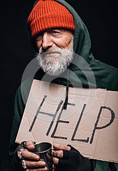 Jobless old beggar holding a handwritten sign for help and a cup for coins