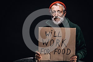 Jobless old beggar holding a handwritten sign for help and money.