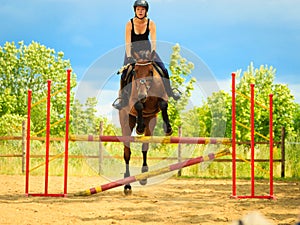 Jockey young girl doing horse jumping through hurdle