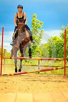 Jockey young girl doing horse jumping through hurdle