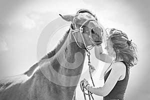 Jockey young girl kissing and hugging brown horse