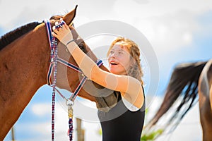 Jockey young girl petting and hugging brown horse