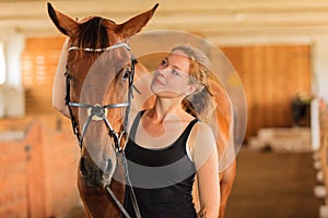 Jockey young girl petting and hugging brown horse