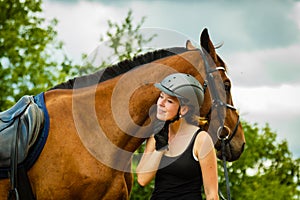 Jockey young girl petting and hugging brown horse