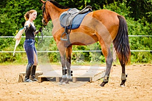 Jockey young woman getting horse ready for ride