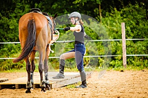 Jockey young woman getting horse ready for ride