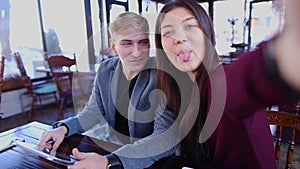 Jocund couple making selfie, using tablet and sticking out tongue.