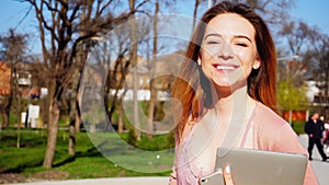 Jocund female person walking on fresh air with laptop and smartp