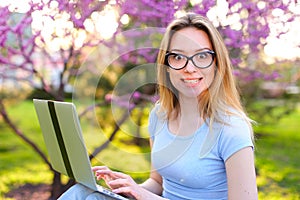 Jocund female person working with laptop in blooming park.