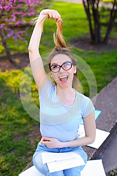 Jocund female student reading papers and playing with hair in spring park.