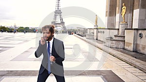 Jocund mulatto guy raving near Eiffel Tower and calling friend by phone in slow motion.