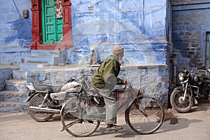 Indian mature man riding a bicycle on the street in old town of blue city Jodhpur, India