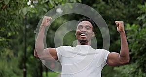 Jogger raising hands in park, slow motion shot. Young African american man first finish triathlon race competition