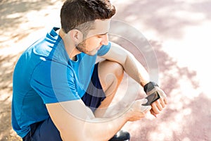 Jogger Syncing Smart Watch With Smartphone While Sitting In Park