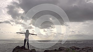 Jogger woman raise hands standing on rock near ocean