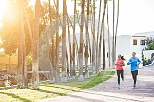 Joggers couple running outdoor in city track with palms in background - Sporty happy people training at sunset in tropical place