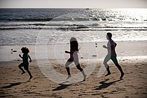 Joggers family have fun on beach run and jump at sunset. Father, mother, baby son run. Child jump with fun by water pool