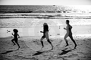 Joggers family have fun on beach run and jump at sunset. Father, mother, baby son run. Child jump with fun by water pool