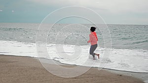 Jogging on beach. Woman runs on sea waves. Running woman on seashore. Motivated sporty female is running at shoreline, waves splas