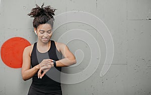 Jogging result. Happy african american girl with wireless headphones checks pulse on fitness bracelet