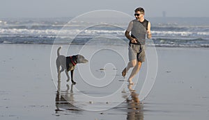 Jogging Summer workout with dog - young attractive and fit runner man training on beautiful beach running barefoot free and happy