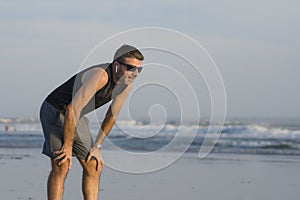 Jogging Summer workout - young attractive and fit runner man training on beautiful beach breathing tired and exhausted cooling off