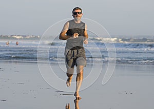 Jogging Summer workout - young attractive and fit runner man training on beautiful beach running barefoot free and happy by the