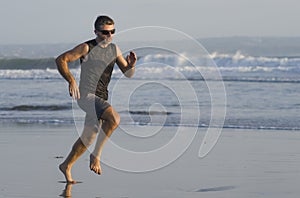 Jogging Summer workout - young attractive and fit runner man training on beautiful beach running barefoot free and happy by the