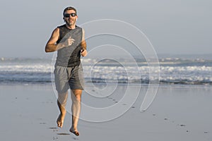 Jogging Summer workout - young attractive and fit runner man training on beautiful beach running barefoot free and happy by the