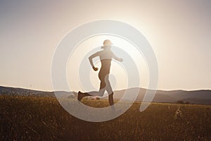 Jogging woman running in summer field at sunset