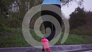 Jogging. A young girl in blue sports clothes is running along the evening park. back view. female legs in sneakers close