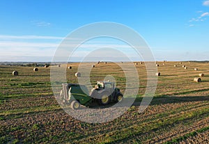 John Deere Tractor 6715R with John Deere V461R round baler making Hay Bales in an agricultural field. Farm Round Hay Bale Tractor