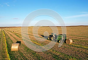 John Deere Tractor 6715R with John Deere V461R round baler making Hay Bales in an agricultural field. Farm Round Hay Bale Tractor