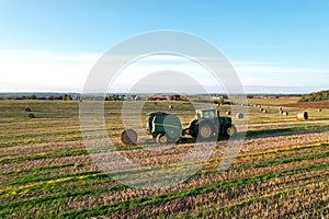John Deere Tractor 6715R with John Deere V461R round baler making Hay Bales in an agricultural field. Farm Round Hay Bale Tractor