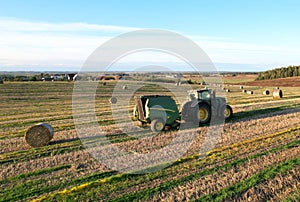 John Deere Tractor 6715R with John Deere V461R round baler making Hay Bales in an agricultural field. Farm Round Hay Bale Tractor